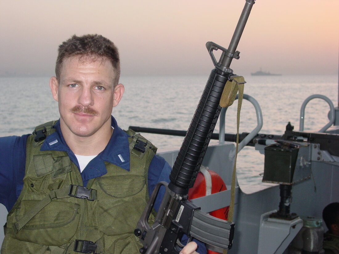 A young Lieutenant Whitmer in body armor aboard a small boat off Kuwait at dusk