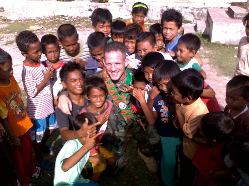 Grant in uniform surrounded by a crowd of laughing children in Micronesia
