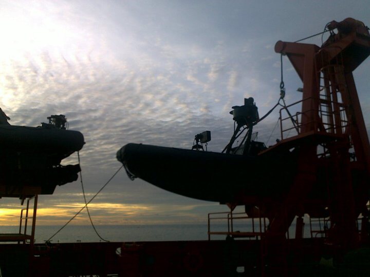 Two rigid-hull inflatable boats silhouetted on their davits at sunset